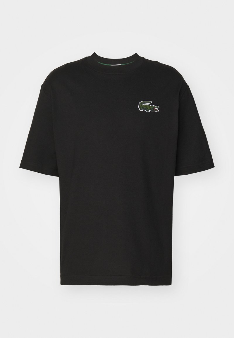 T-shirt noir à manches courtes avec col rond et petit logo crocodile vert sur le côté gauche de la poitrine sur fond uni.