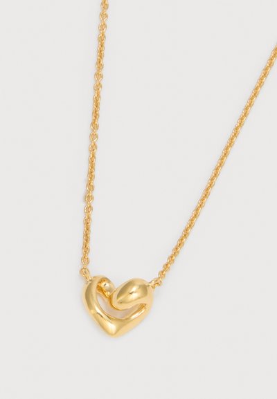 Χρυσό κολιέ με αλυσίδα και κρεμαστό σε σχήμα καρδιάς που διαθέτει αφηρημένο, καμπυλωτό σχέδιο σε ουδέτερο φόντο.