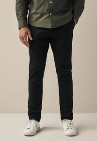 Grüne Button-Down-Hemd mit Kragen, schwarze Slim-Fit-Hosen und weiße Sneaker. Glattes Material, keine sichtbaren Muster oder Akzente.