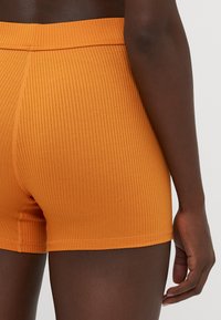 Pantaloni corti arancioni a costine con una texture morbida e una vita elastica. I dettagli delle cuciture sono visibili lungo i bordi.