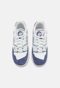 Ténis brancos e azul marinho com um bico em camurça texturizada, parte superior em malha e pormenores em cinza. Apresentam atacadores e um logótipo circular na língua.