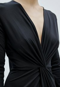 Schwarzes Langarmkleid mit tiefem V-Ausschnitt und gerafftem Detail an der Taille. Glatter Stoff mit leichtem Glanz und taillierter Silhouette.
