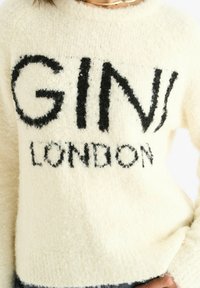 Person wearing a fuzzy white sweater with "GIVI LONDON" in large black letters on the front and a thin gold necklace visible.
