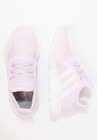 Světle růžové atletické tenisky s bílou podrážkou a třemi bílými pruhy na bocích, zobrazené z vrchu a z bočního úhlu.