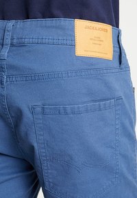 Blå denimbyxor med en märkesläderetikett, bakficka med sömdetaljer och slät textur. Enkla i designen utan mönster.