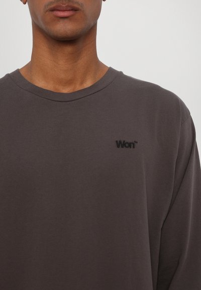 Szürke, hosszú ujjú, puha pamut póló, crew neck nyakkivágással és egy kis fekete hímzett logóval a bal mellrészen.