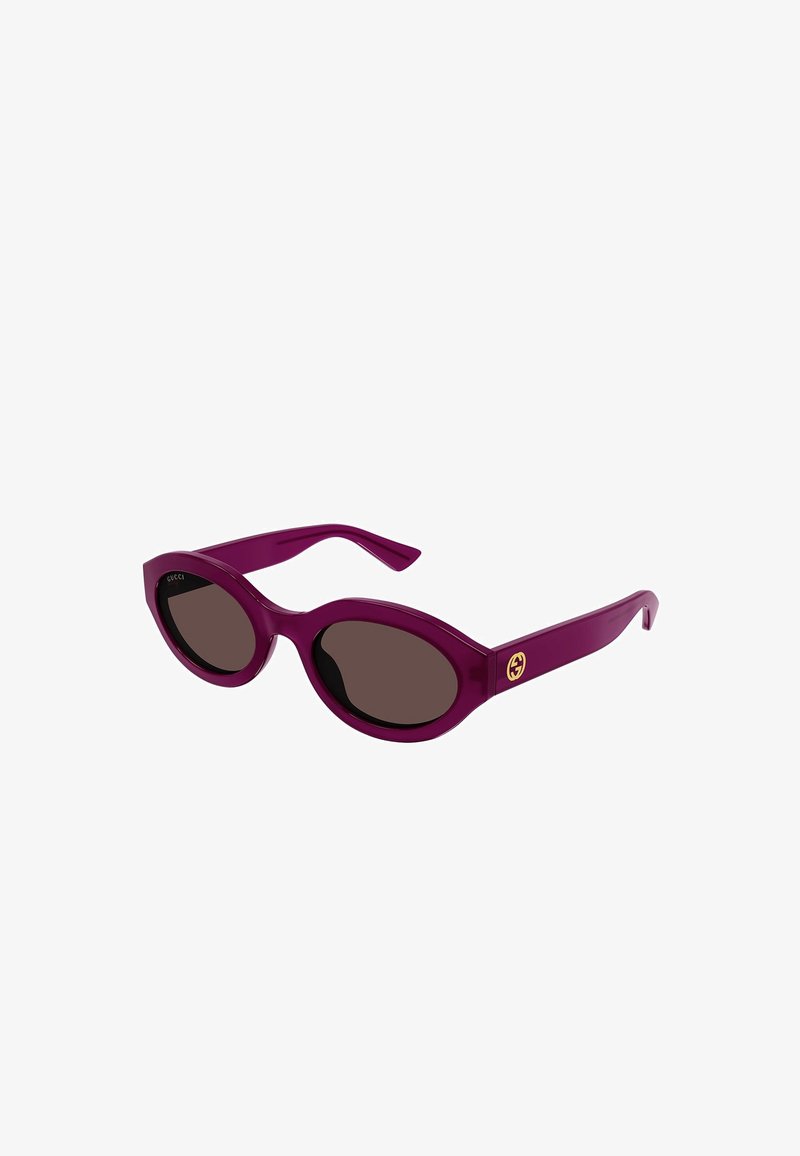 Violetās plastmasas saulesbrilles ar brūniem lēcām, ovālas formas, un zelta logotipa detaļa uz kājas. Gluda tekstūra ar spīdīgu apdari.