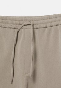 Pantalon de survêtement beige clair avec une taille élastique et un cordon de serrage. Le tissu est lisse avec des détails de coutures discrètes.