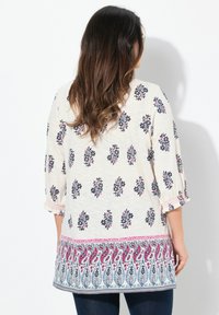 Lys creme farvet top med blomsterprint i marineblå og pink, med en paisley kant og trekvartlang ærmer. Tekstureret stof.