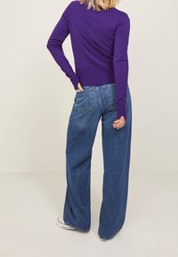 Pull ajusté violet associé à un jean denim bleu à jambes larges. Le jean comporte des poches arrière et une silhouette décontractée. Design simple, look casual.