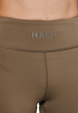 Zbliżenie na pas beżowych legginsów sportowych z logo "HALO" i widocznym przeszyciem na tle nagiej skóry.