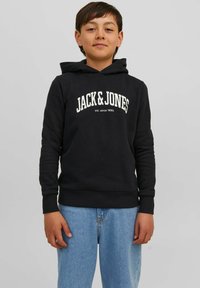 Sudadera negra con un logo frontal "JACK & JONES" en blanco, puños y dobladillo acanalados, combinada con unos jeans de mezclilla azul claro.