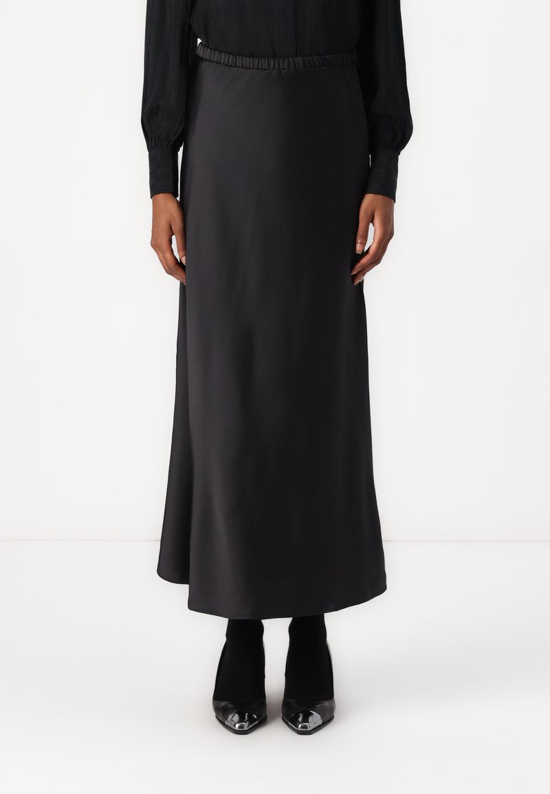 Svart, ankellangskjørt med elastisk linning i glatt stoff. Kombinert med svarte, spisse heels. Enkel og stilren design.