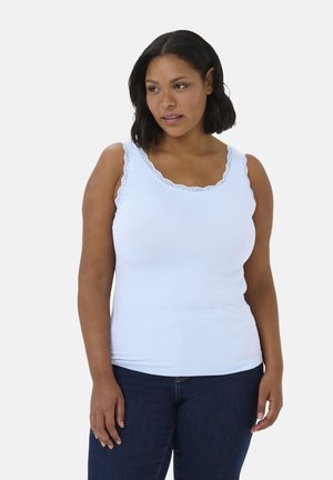 Weißes, geripptes Tanktop mit einem gewellten Spitzenbesatz, das eine figurbetonte Passform und breite Träger aufweist. Das Modell trägt es zu einer dunklen Jeans.