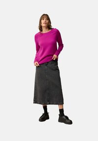Roze gebreide trui met ronde halslijn en lange mouwen, gecombineerd met een zwarte denim maxi-skirt en zwarte veterschoenen.