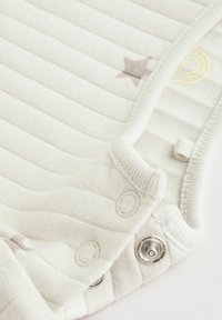 Rugbrun i lys grå med horisontale ribbede strukturer. Har metal trykknapper og små trykte stjerne- og regnbue-designs.