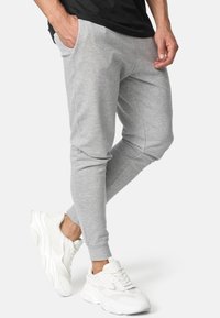 Graue Jogginghosen aus weichem Material, mit schmal zulaufenden Beinen, Seitentaschen und elastischen Bündchen, kombiniert mit weißen Sneakern.