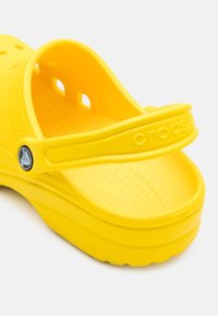 Yellow rubber clog featuring a thick band, multiple ventilation holes, textured tread, and embossed branding on the strap.