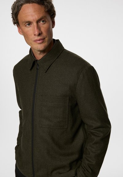 Mörkgrön zip-up jacka med krage, en bröstficka och texturerad tyg som visar en strukturerad, smal passform.