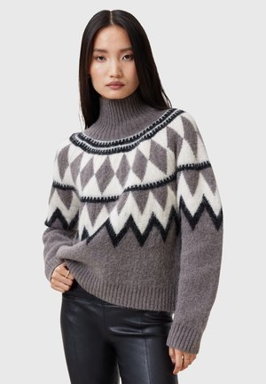 Grau gestrickter Pullover mit einem hohen, gerippten Kragen, der ein geometrisches Muster in Weiß und Schwarz zeigt. Das Design umfasst Zickzack- und Rautenmuster.