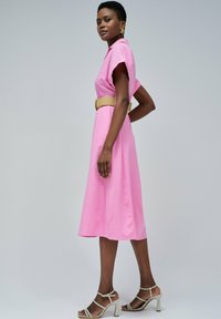 Rosa Midi-Kleid mit kurzen Ärmeln, tailliertem Schnitt und glatter Oberfläche. Kombiniert mit beigen hohen Sandalen. Bodenlanger Silhouette.