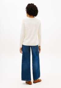 Άσπρο πλεκτό πουλόβερ με ριγέ υφή συνδυασμένο με μπλε τζιν παντελόνια φαρδιάς γραμμής. Τα τζιν έχουν ξεθωριασμένη υφή και κανονικό τελείωμα. Καφέ δερμάτινα παπούτσια ολοκληρώνουν το σύνολο.