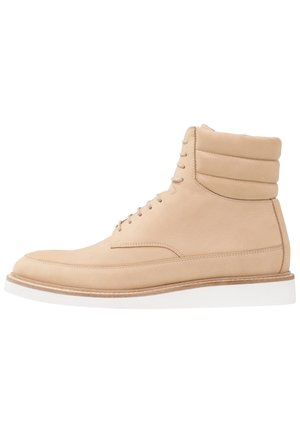 Light beige leather ankle boots with padded collar, lace-up front, and a white rubber sole, featuring a smooth texture and minimalistic design.