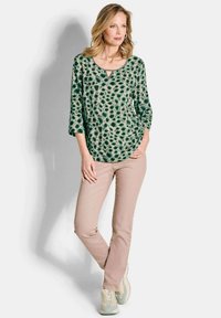 Top verde con stampa animale, scollatura a giro e maniche a tre quarti, abbinato a pantaloni beige chiaro e sneakers. Tessuto morbido e liscio.