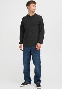 Suéter de punto gris oscuro con textura acanalada, cuello redondo y hombros caídos, combinado con jeans azules de pierna recta y zapatillas negras.