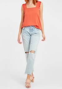 Orange ärmlös topp med volangaxlar, matchad med ljusblå slitna jeans med rivna knän och fransar vid fållen, kompletterad med beige klackar.