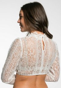 Witte kant blouse met lange mouwen, hoge hals en een opening op de rug. Kenmerken zijn bloemmotieven en een semi-doorzichtige textuur.