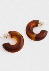 Καφέ ρητίνες σκουλαρίκια σε σχήμα κρίκων με ημιδιαφανές φινίρισμα και χρυσές λεπτομέρειες. Καμπυλωτός, σύγχρονος σχεδιασμός με γυαλιστερή επιφάνεια.