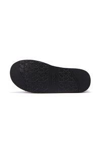 Suela de zapato de goma negra con patrones texturizados y una sutil marca, con un talón liso y un diseño plano para mayor estabilidad.