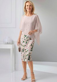 Blush Chiffon-Overlay-Oberteil kombiniert mit einem blumendruckierten Bleistiftrock, der grüne Blätter und weiße Magnolienblüten zeigt. Beigefarbene Block-Absatzsandalen.