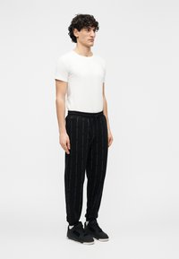 Pantalones de chándal negros con un patrón de texto repetido, cintura elástica y puños. Combinados con una camiseta blanca ajustada y zapatillas negras.