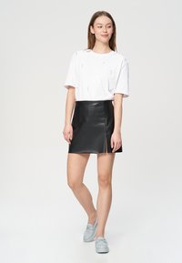 Biała bawełniana koszulka z małymi ozdobami, zestawiona z czarną spódnicą mini z imitacji skóry, z bocznym rozcięciem, noszona z jasnoniebieskimi loafersami.
