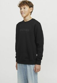 Svart bomullströja med prägling "ORIGINALS" på framsidan, med ribbade manschetter och nederkant, i kombination med ljusblå denimbyxor.