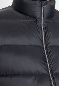 Svart pufferjacka med hög krage, horisontellt quiltat mönster och silverfärgad dragkedja. Materialet verkar slätt och isolerat.