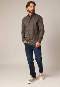 Donker geblokt overhemd met lange mouwen, gedragen met een blauwe spijkerbroek en beige schoenen met lage schacht. Glad materiaal en standaard pasvorm.