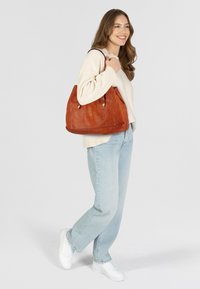 Borsa in pelle arancione con una texture morbida, dotata di due manici corti, dettagli in hardware dorato e una forma triangolare strutturata.