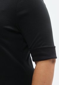 Top negru cu mâneci scurte și tiv întors, realizat dintr-un material neted și elastic. Prezintă un croi mulat și o siluetă curată, minimalistă.