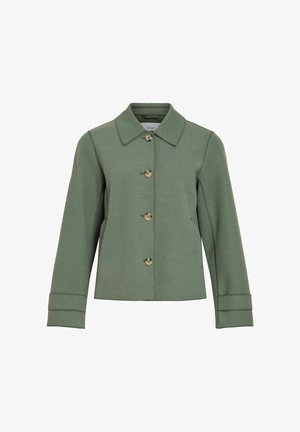 Roheline villa segu jope terava krae, nuppude kinnituse ja pruunide nuppudega, pikkade varrukatega, mille mansetid on üles keeratud.