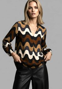 Langärmlige Bluse mit wellenförmigem Muster in Braun, Creme und Schwarz. V-Ausschnitt und Ärmelenden mit Manschetten aus leichtem Stoff.