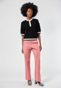 Camisa polo de punto acanalado negra con detalles en crema, combinada con pantalones de pierna ancha rosas con rayas laterales. La modelo lleva tacones adornados.