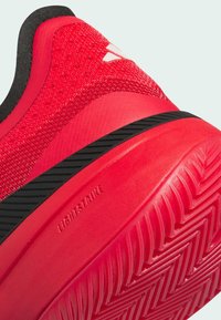 Gros plan du talon d’une chaussure de sport rouge avec une semelle texturée, un détail de bande noire et « Lightstrike » embossé sur la semelle intermédiaire.