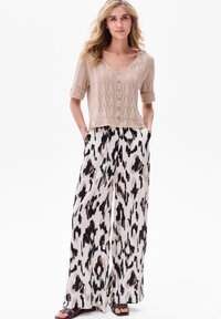 Beżowy, dziany top na krótki rękaw z dekoltem w serek i teksturowanym wzorem, połączony z szerokimi spodniami w czarno-różowy abstrakcyjny wzór.