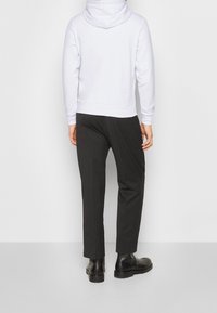 Felpa bianca con cappuccio, dotata di orlo posteriore e polsini, abbinata a pantaloni neri eleganti e stivali neri alla caviglia. Tessuto morbido con una vestibilità comoda.