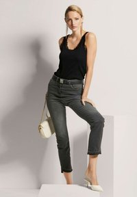 Zwarte tanktop met kantafwerking, grijze jeans met een cropped zoom, witte high-heel schoenen en een crèmekleurige handtas met een kettingriem.