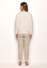 Cream pullover with a relaxed fit and ribbed hem, paired with tapered beige pants featuring a subtle leopard pattern.