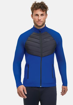 Blauwe sportjack met lange mouwen, ritssluiting en een textuur paneel van zwart padding op de borst. Voorzien van dubbele zijzakken en een hoge kraag.